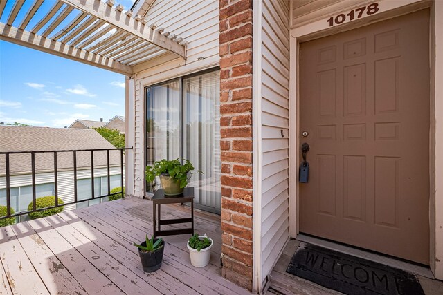 view of exterior entry featuring a pergola, a balcony, and brick siding