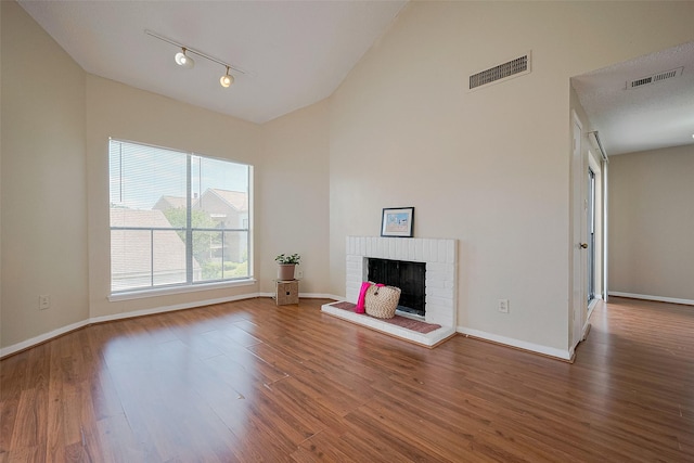 unfurnished living room featuring a brick fireplace, visible vents, rail lighting, and wood finished floors