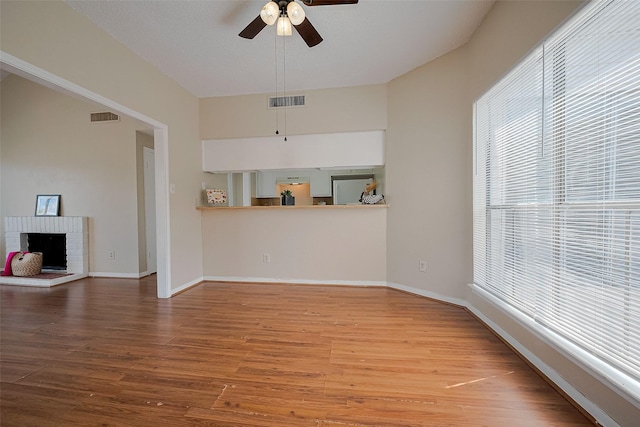 unfurnished living room with a ceiling fan, visible vents, wood finished floors, and baseboards