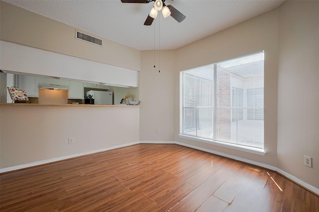 empty room with visible vents, ceiling fan, wood finished floors, and baseboards