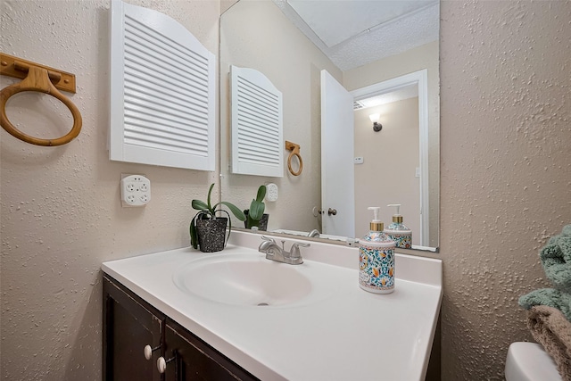 bathroom with toilet, a textured wall, and vanity