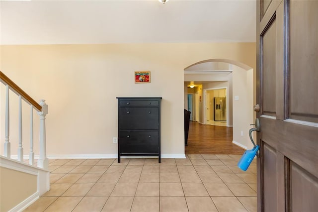 foyer with arched walkways, light tile patterned floors, baseboards, and stairway