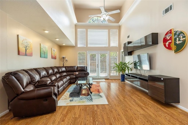 living area with a ceiling fan, visible vents, a high ceiling, wood finished floors, and baseboards