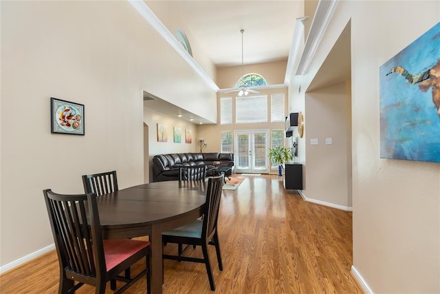 dining space featuring light wood finished floors, a high ceiling, baseboards, and ceiling fan