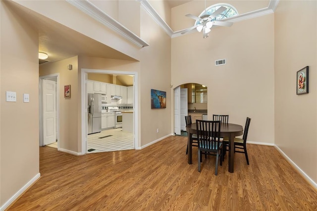 dining space featuring light wood-type flooring, baseboards, visible vents, ceiling fan, and arched walkways