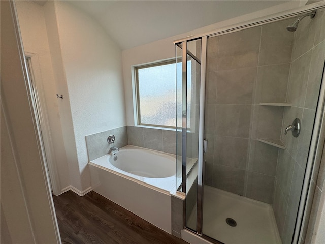 bathroom featuring lofted ceiling, wood finished floors, baseboards, a garden tub, and a stall shower