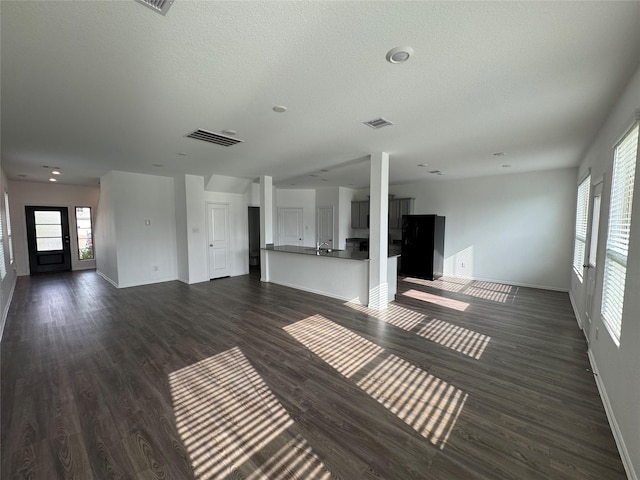 unfurnished living room featuring baseboards, dark wood-style flooring, and visible vents