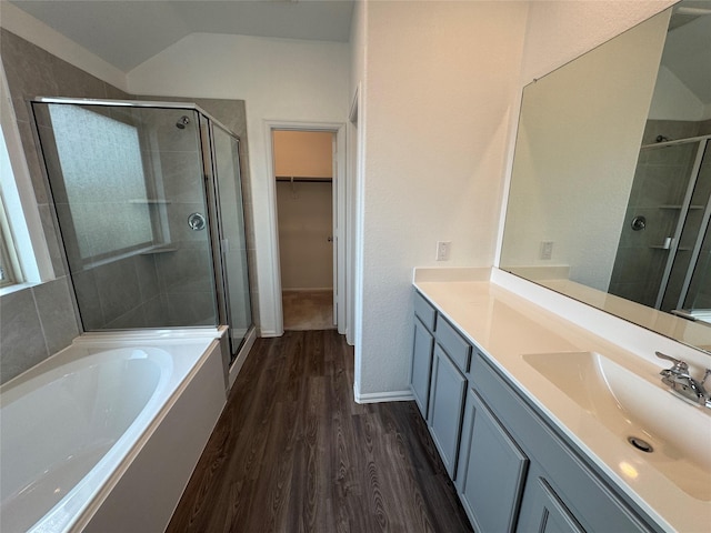full bathroom featuring vaulted ceiling, wood finished floors, a stall shower, a walk in closet, and vanity