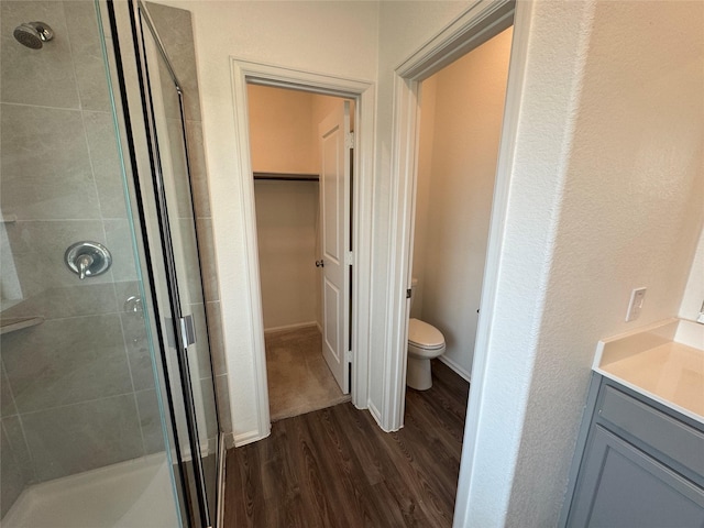 full bath featuring toilet, a spacious closet, wood finished floors, a shower stall, and vanity