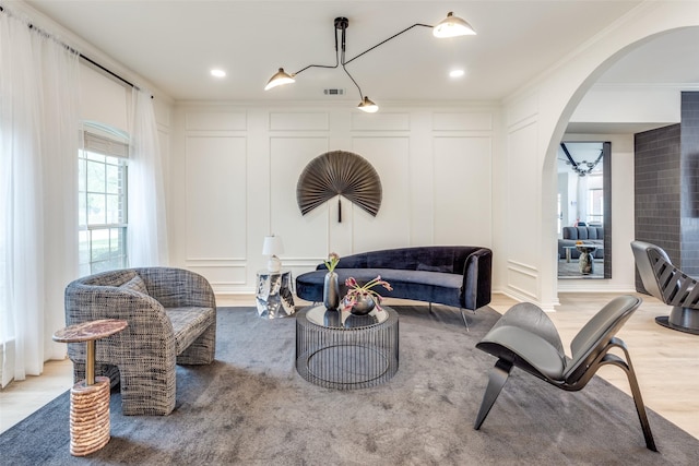 sitting room with arched walkways, a decorative wall, visible vents, and crown molding