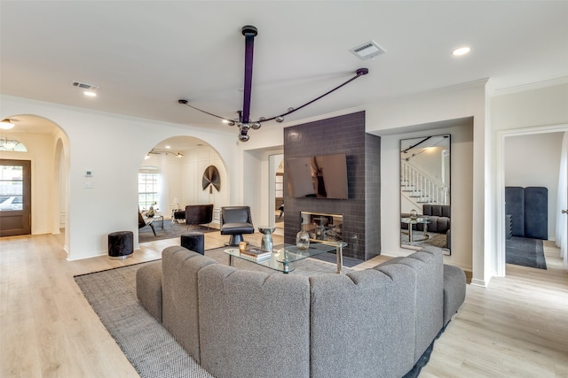 living area featuring ornamental molding, visible vents, light wood-style flooring, and arched walkways