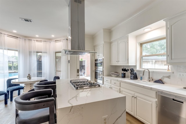 kitchen with visible vents, a sink, appliances with stainless steel finishes, island exhaust hood, and light stone counters