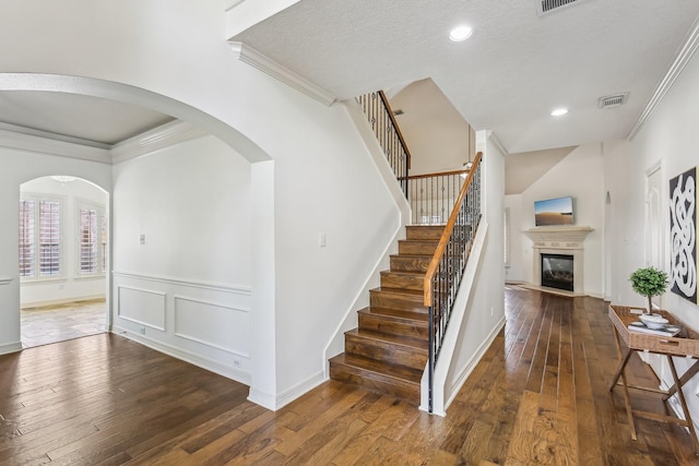 15614 Stone Gables Ln, Houston, TX 77044 - stairway featuring crown molding, hardwood / wood-style flooring, a glass covered fireplace, arched walkways, and wainscoting