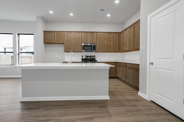 kitchen with a sink, a center island with sink, appliances with stainless steel finishes, dark wood-type flooring, and visible vents