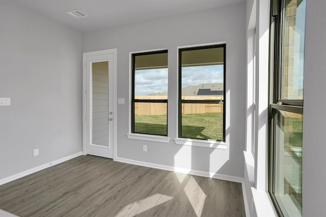 unfurnished room featuring wood finished floors, visible vents, baseboards, and plenty of natural light