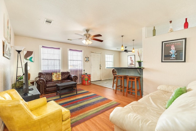 living room featuring visible vents, baseboards, a ceiling fan, and wood finished floors