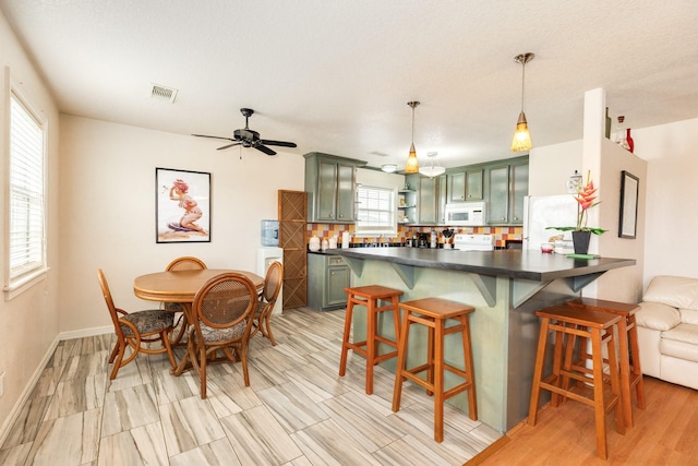 kitchen featuring visible vents, green cabinetry, a breakfast bar, dark countertops, and white appliances