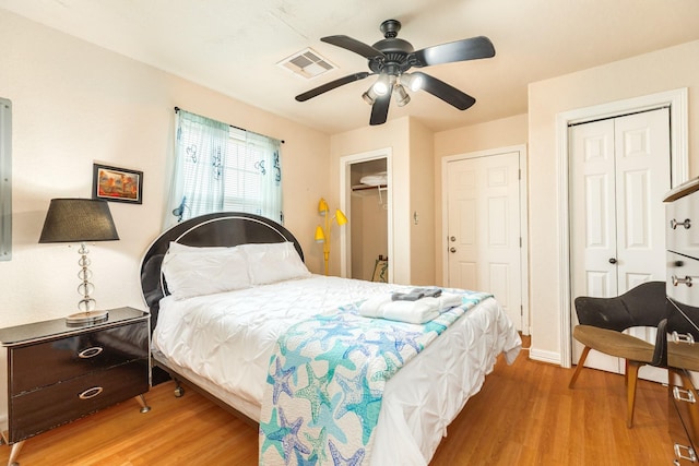bedroom with multiple closets, visible vents, a ceiling fan, and wood finished floors
