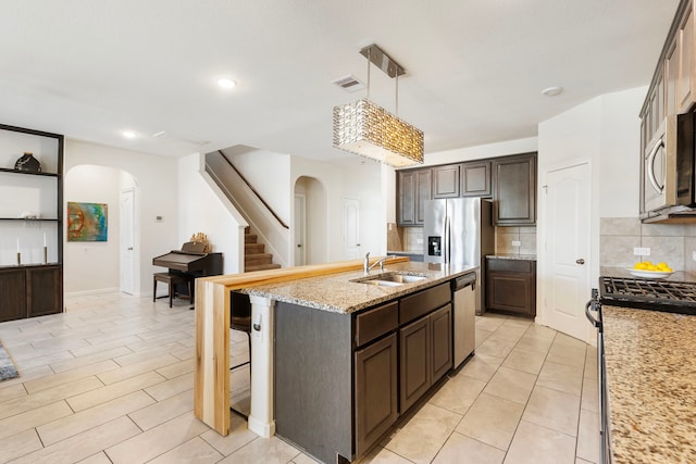 12420 Southern Trail Ct, Magnolia, TX 77354 - kitchen with arched walkways, a sink, dark brown cabinets, and appliances with stainless steel finishes