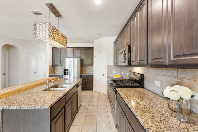 12420 Southern Trail Ct, Magnolia, TX 77354 - kitchen with tasteful backsplash, a sink, appliances with stainless steel finishes, dark brown cabinets, and light stone counters