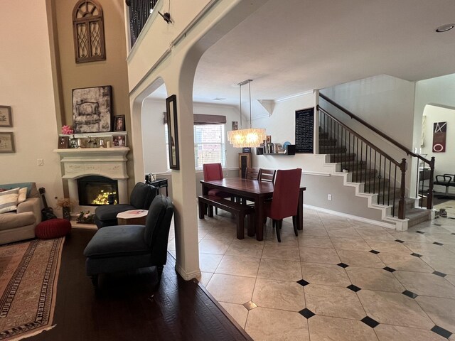 tiled dining area with an inviting chandelier, baseboards, a warm lit fireplace, stairway, and arched walkways