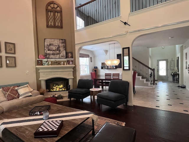 living room with arched walkways, a high ceiling, a warm lit fireplace, and a chandelier