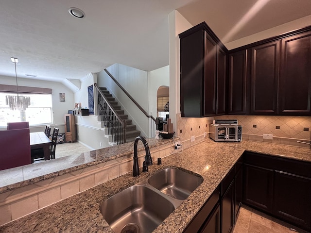 kitchen featuring an inviting chandelier, a sink, arched walkways, stone countertops, and decorative backsplash