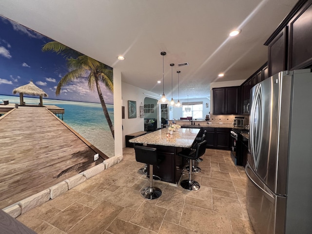 kitchen featuring stone tile flooring, freestanding refrigerator, a kitchen island, light stone countertops, and a kitchen bar
