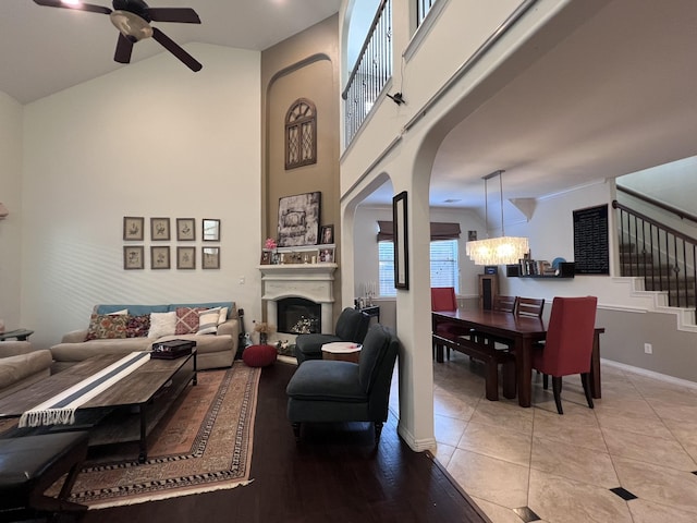 living room with arched walkways, high vaulted ceiling, ceiling fan with notable chandelier, stairs, and baseboards