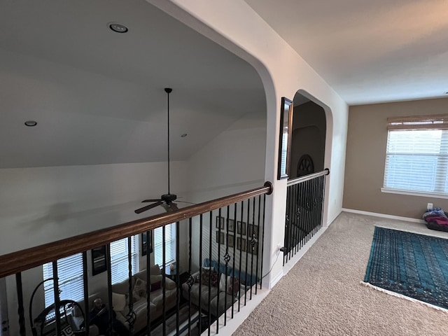 hall featuring baseboards, carpet, and arched walkways