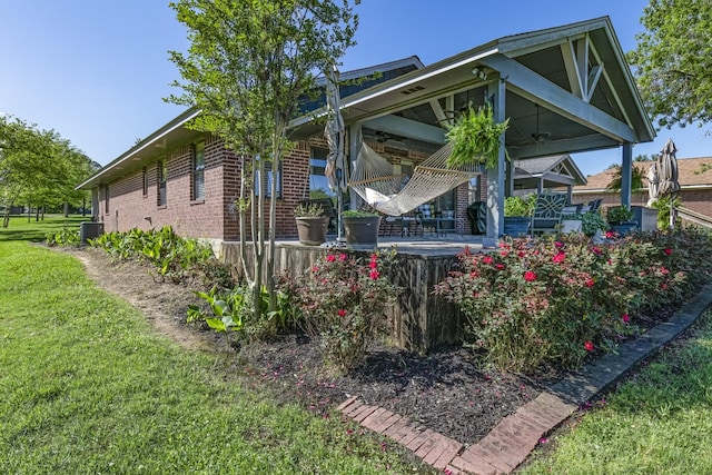 view of side of property featuring brick siding, a yard, a ceiling fan, and cooling unit