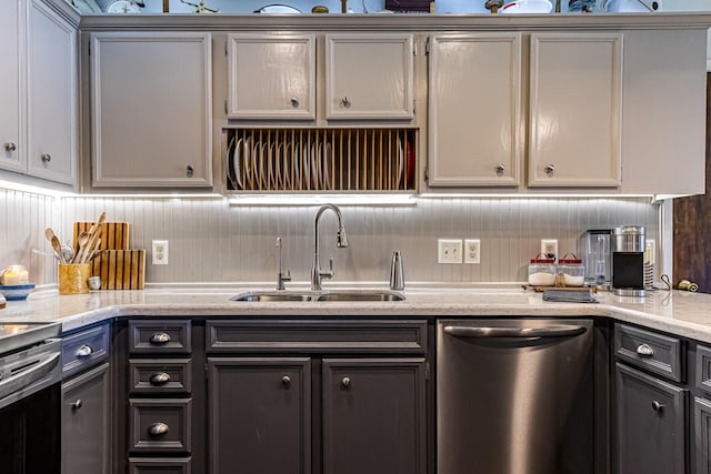 kitchen with appliances with stainless steel finishes, gray cabinets, light stone counters, and a sink