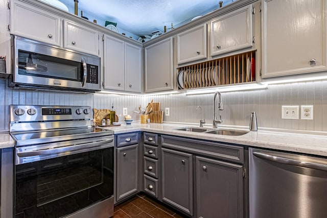kitchen featuring light stone countertops, stainless steel appliances, gray cabinetry, and a sink