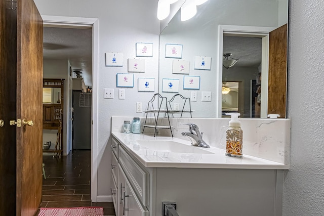 bathroom with a textured ceiling, wood finished floors, ceiling fan, a textured wall, and vanity
