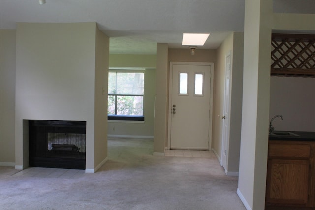 entryway featuring light carpet, baseboards, a multi sided fireplace, and a skylight