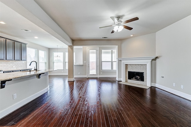 unfurnished living room featuring a fireplace, a ceiling fan, visible vents, dark wood-style flooring, and baseboards