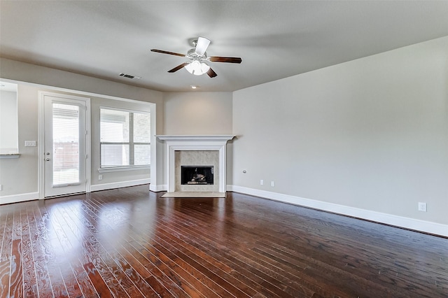 unfurnished living room with a tiled fireplace, dark wood-style floors, baseboards, and a ceiling fan