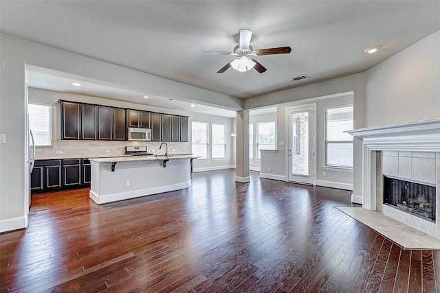 unfurnished living room with ceiling fan, baseboards, visible vents, and dark wood-style flooring