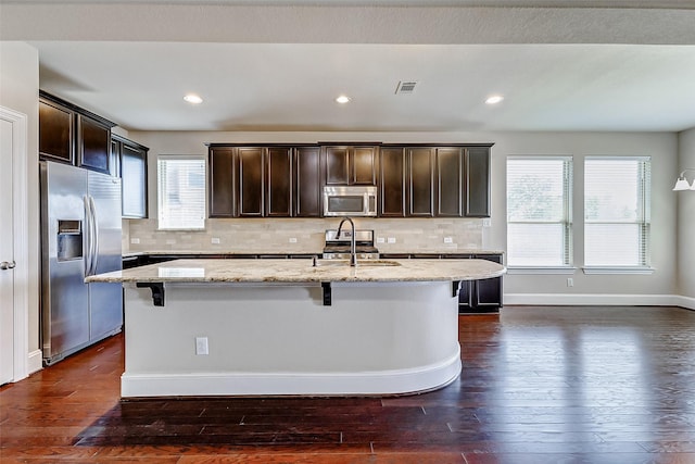 kitchen with light stone countertops, visible vents, a kitchen bar, appliances with stainless steel finishes, and a sink