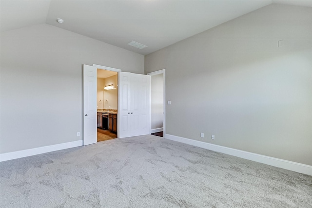 unfurnished bedroom featuring ensuite bath, visible vents, carpet flooring, lofted ceiling, and baseboards
