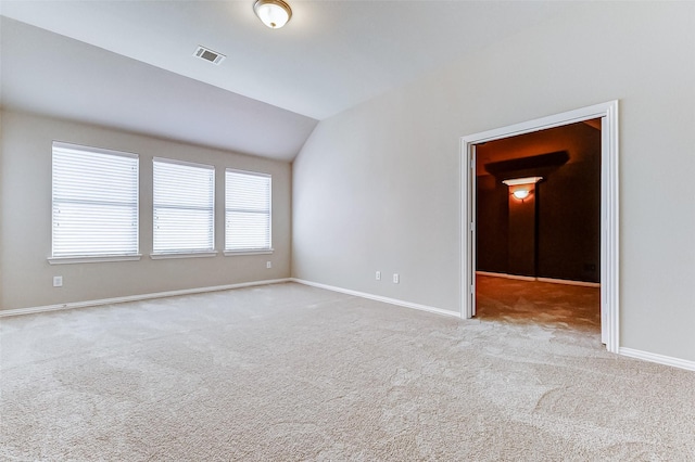carpeted spare room featuring baseboards, vaulted ceiling, and visible vents