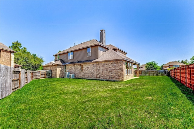 rear view of house with brick siding, a fenced backyard, a chimney, and a lawn