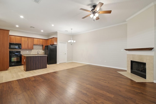 kitchen with light wood-style flooring, black appliances, a center island, a tiled fireplace, and open floor plan