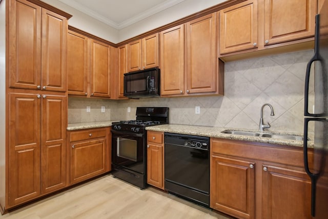kitchen with a sink, ornamental molding, black appliances, backsplash, and light stone counters