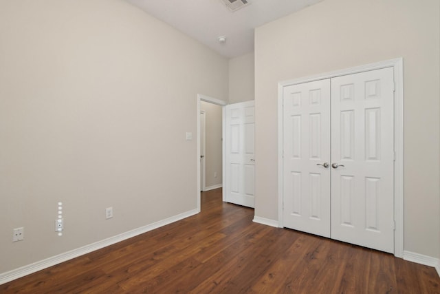 unfurnished bedroom featuring a closet, visible vents, baseboards, and dark wood finished floors