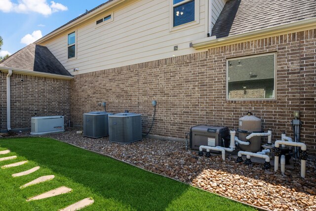 back of house featuring central AC unit, a shingled roof, and brick siding