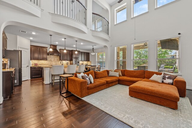 living area featuring dark wood-style flooring, plenty of natural light, a high ceiling, visible vents, and arched walkways