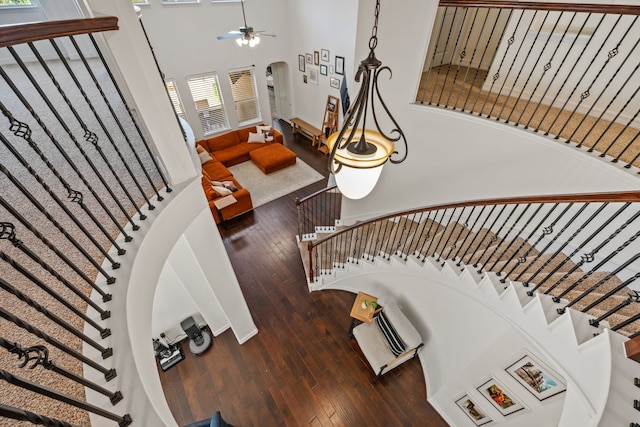 staircase with arched walkways, a high ceiling, ceiling fan, and hardwood / wood-style flooring