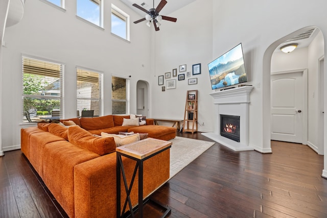 living area with a ceiling fan, arched walkways, a towering ceiling, and a healthy amount of sunlight