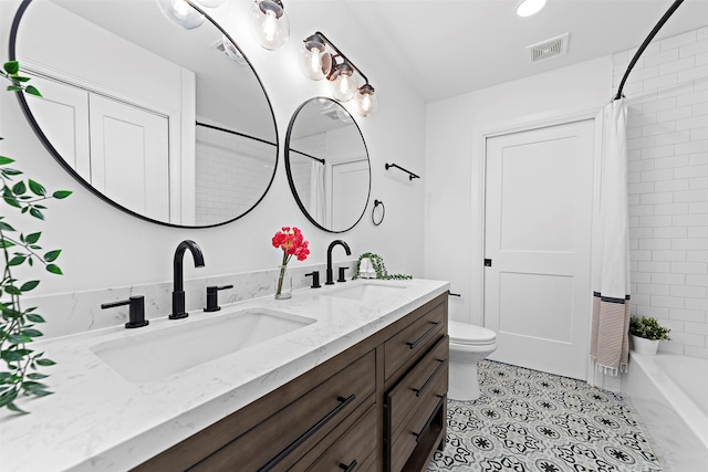 bathroom featuring toilet, double vanity, a sink, and visible vents
